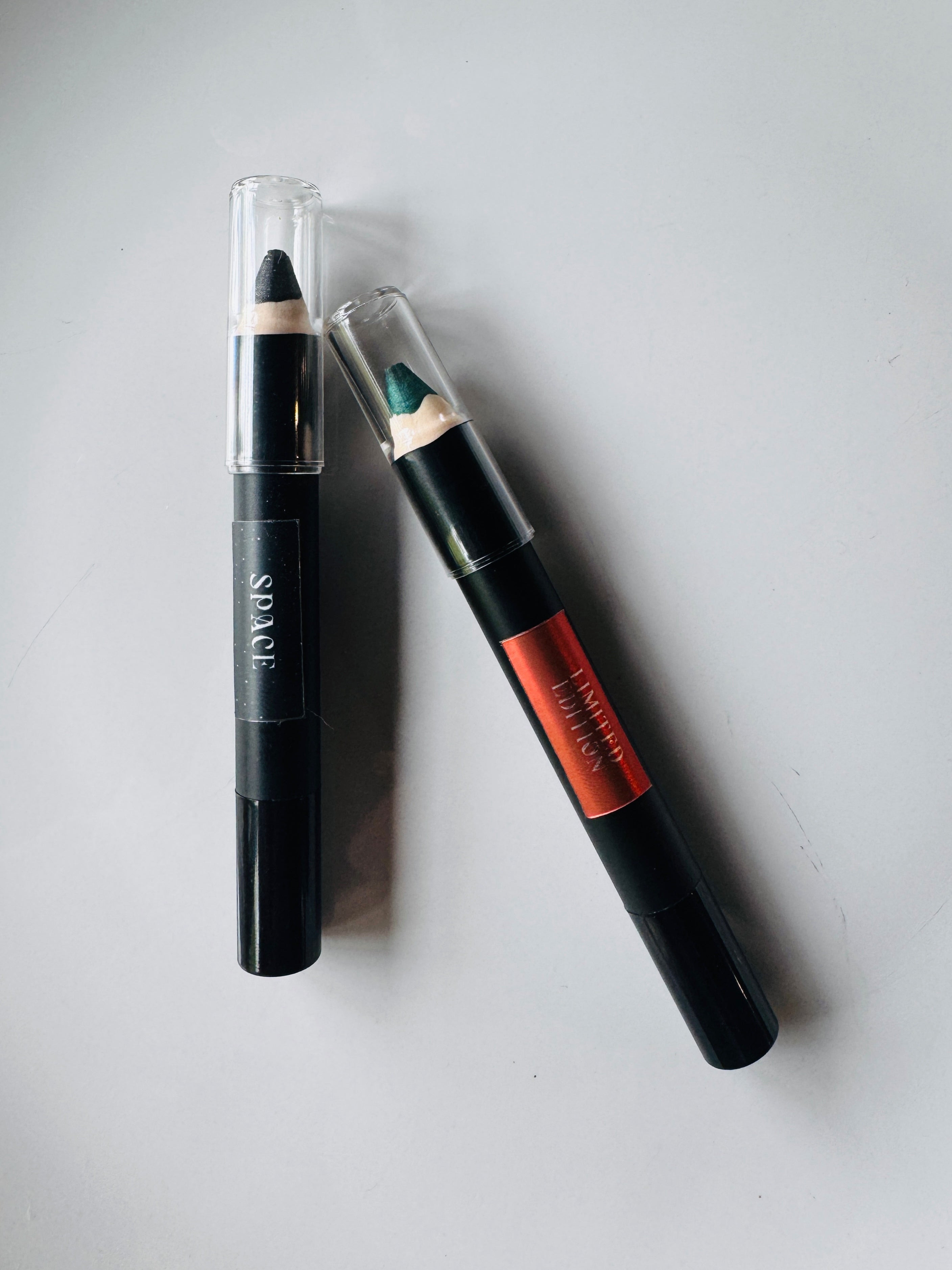 Two makeup pencils with black and orange packaging on a light gray background
