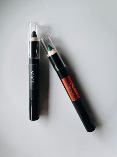 Two makeup pencils with black and orange packaging on a light gray background