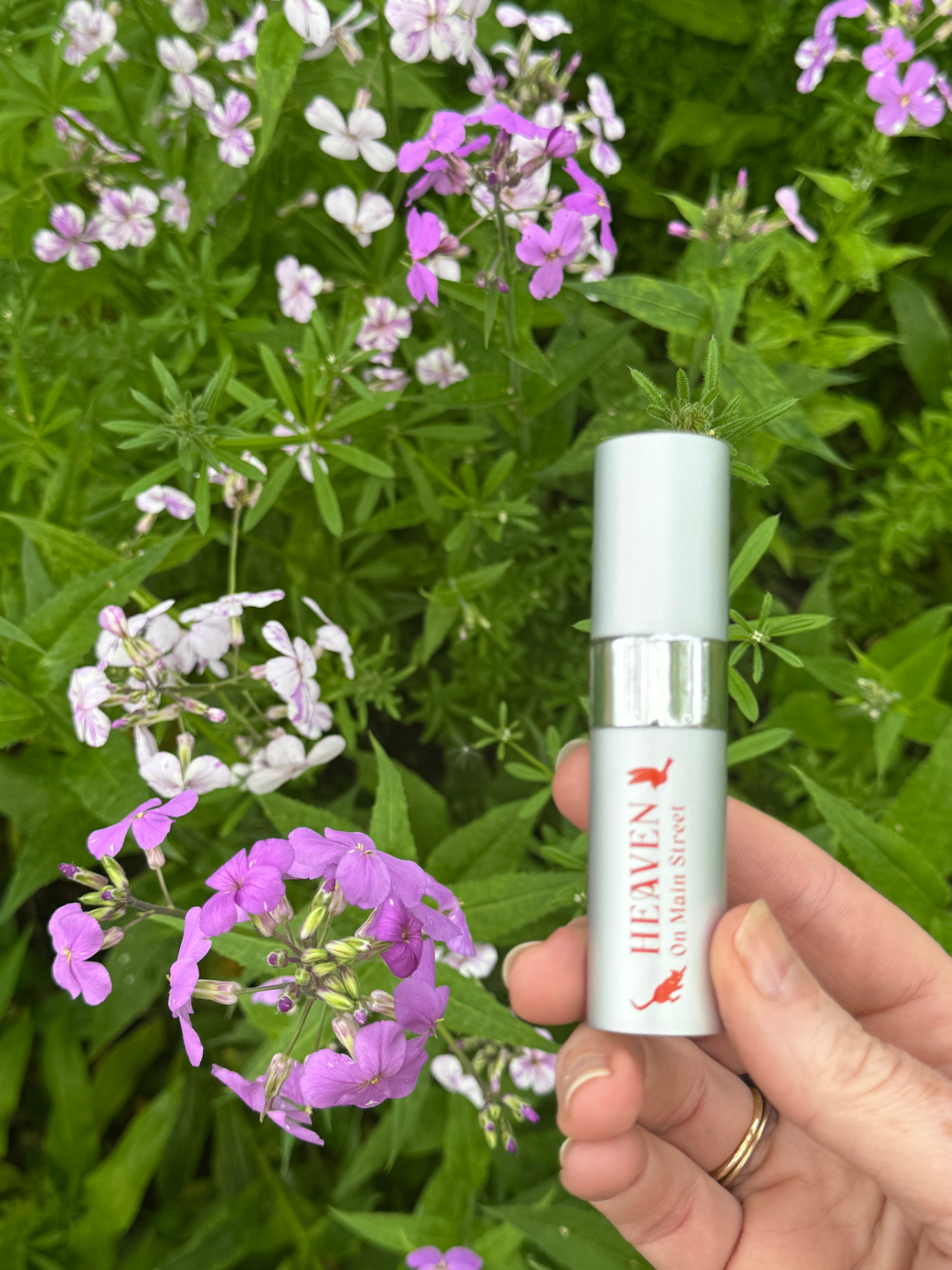 Hand holding a small bottle labeled 'Heaven' among flowers